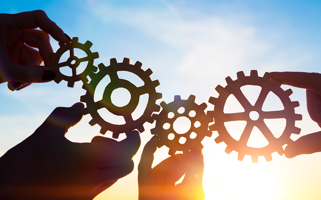 Four businessmen's hands assembling gears and puzzle pieces, symbolizing teamwork and collaboration.
