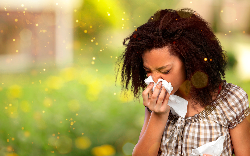 Young woman sneezing into a tissue outdoors during allergy season.